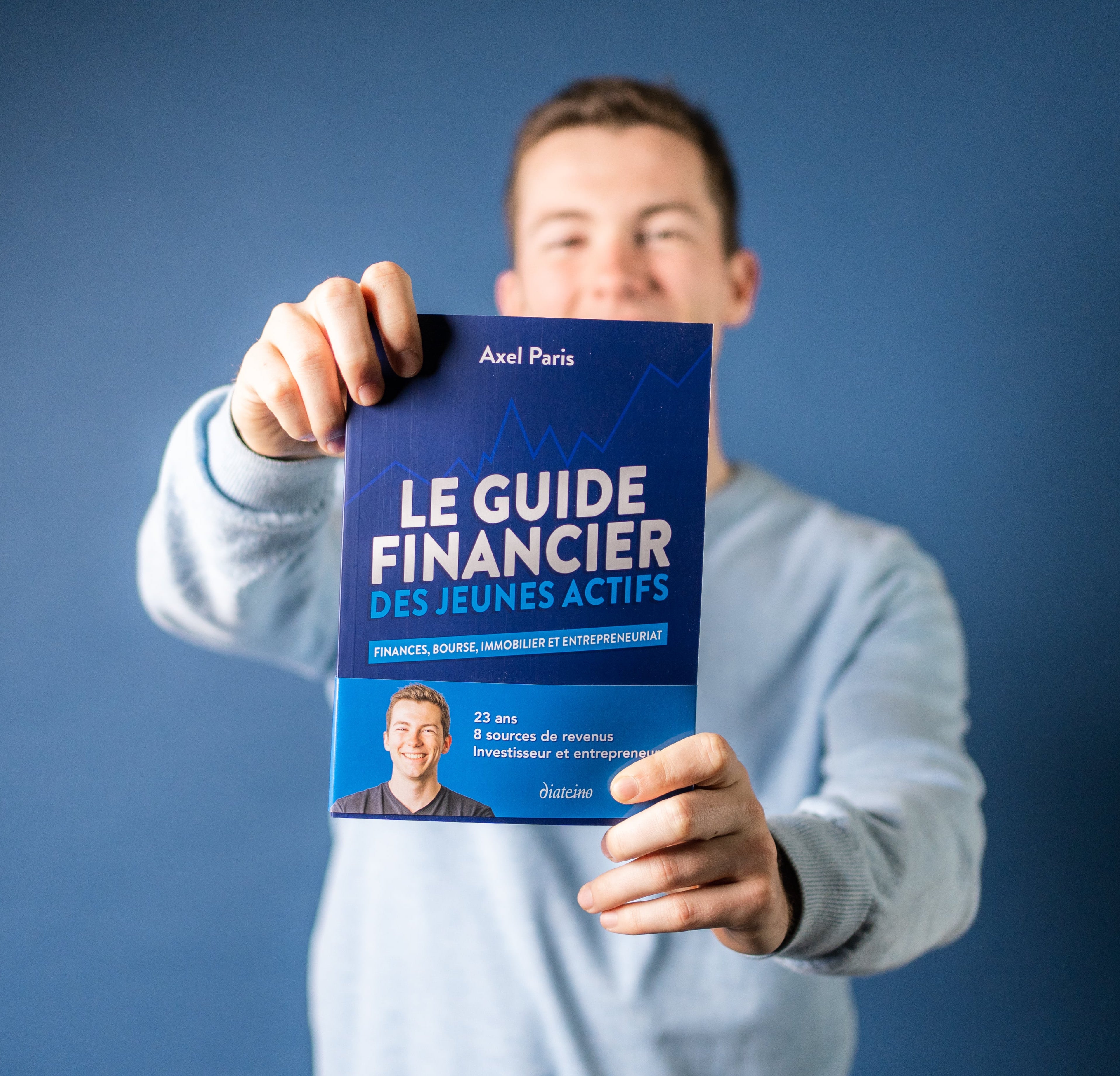 Photo d'Axel Paris qui tient son livre "Le guide financier des jeunes actifs" dans les mains